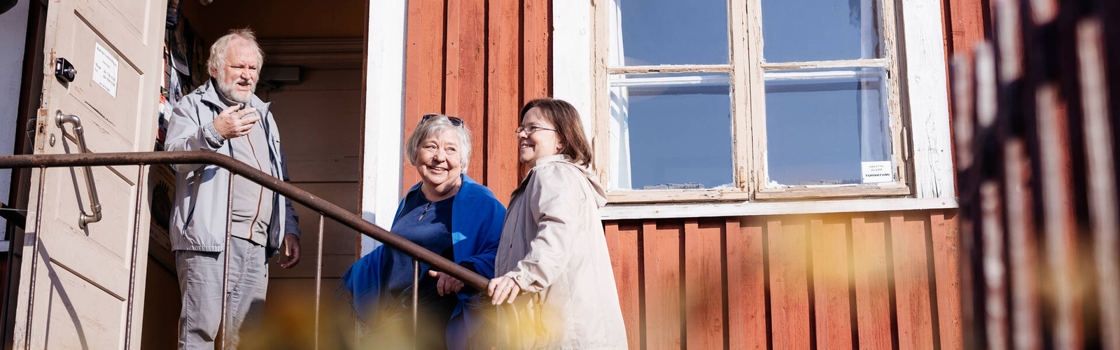Kolme ihmistä hymyilee talon edessä olevilla rappusilla.